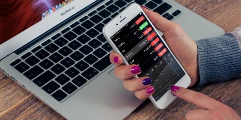 a person with painted nails is using a mobile phone with laptop on a wooden-table