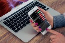 a person with painted nails is using a mobile phone with laptop on a wooden-table